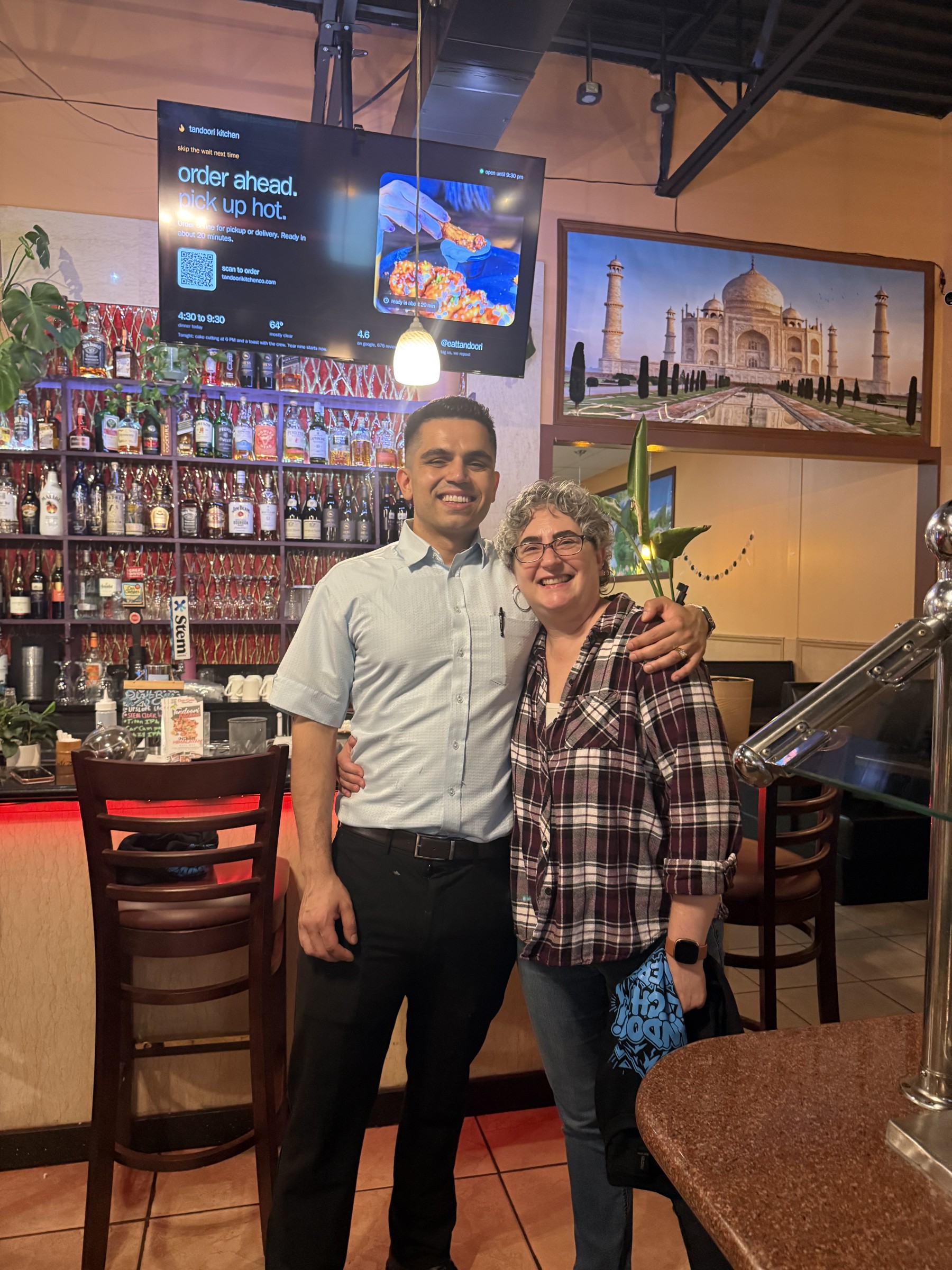 A guest and a Tandoori Kitchen team member pose by the bar.
