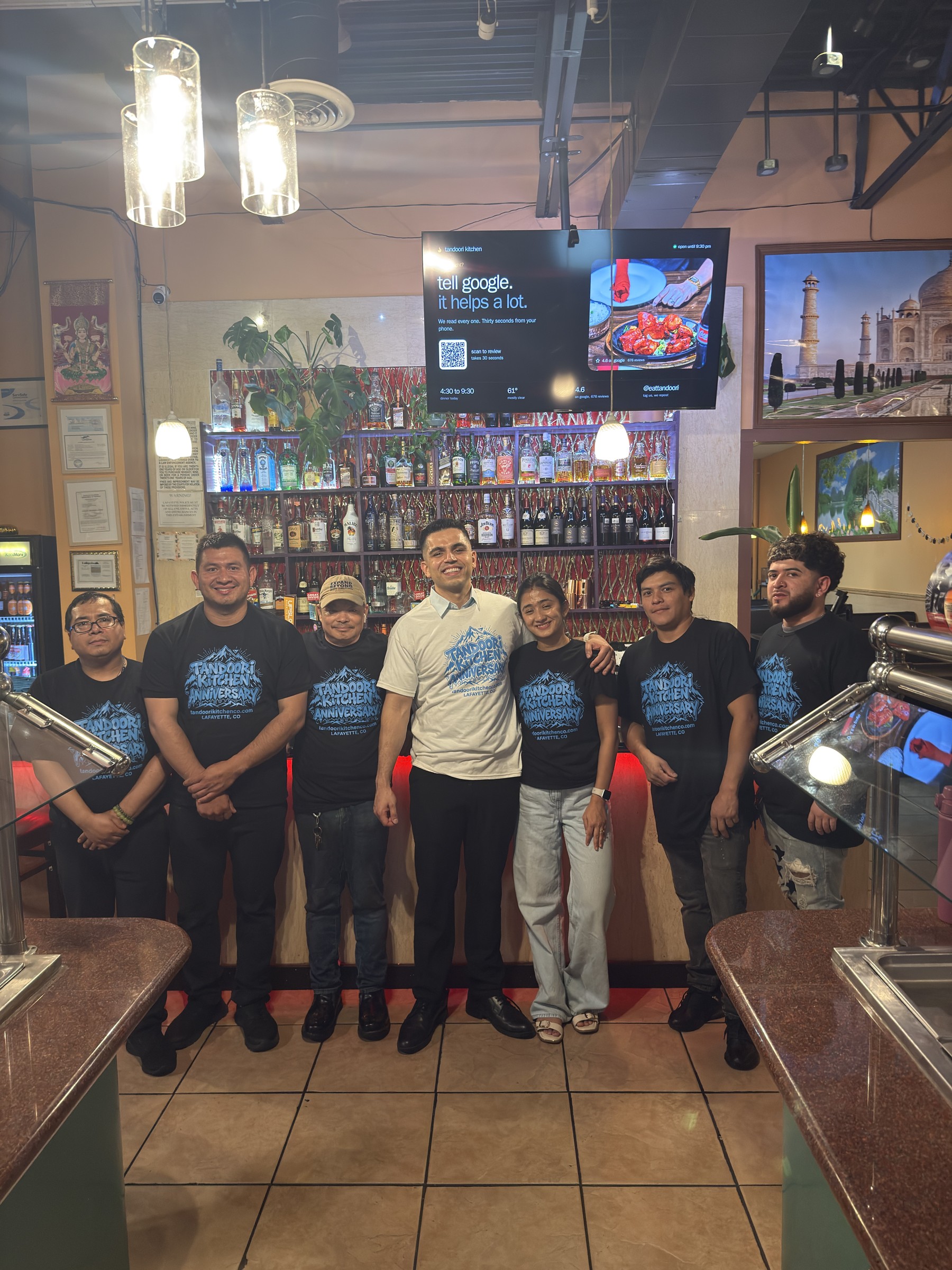 The Tandoori Kitchen team lined up in the dining room wearing anniversary tees.
