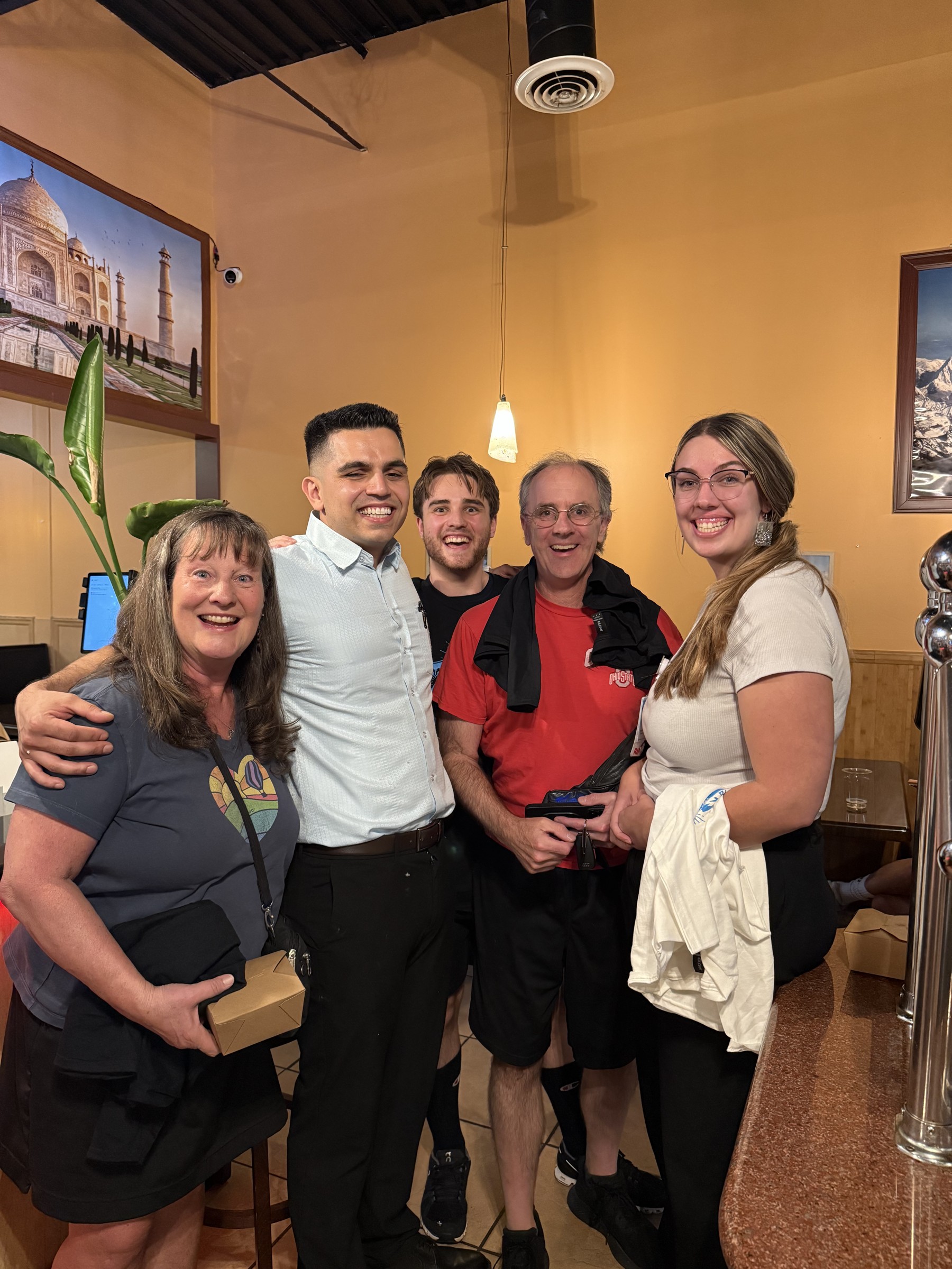 A group of guests smiles with a Tandoori Kitchen team member.